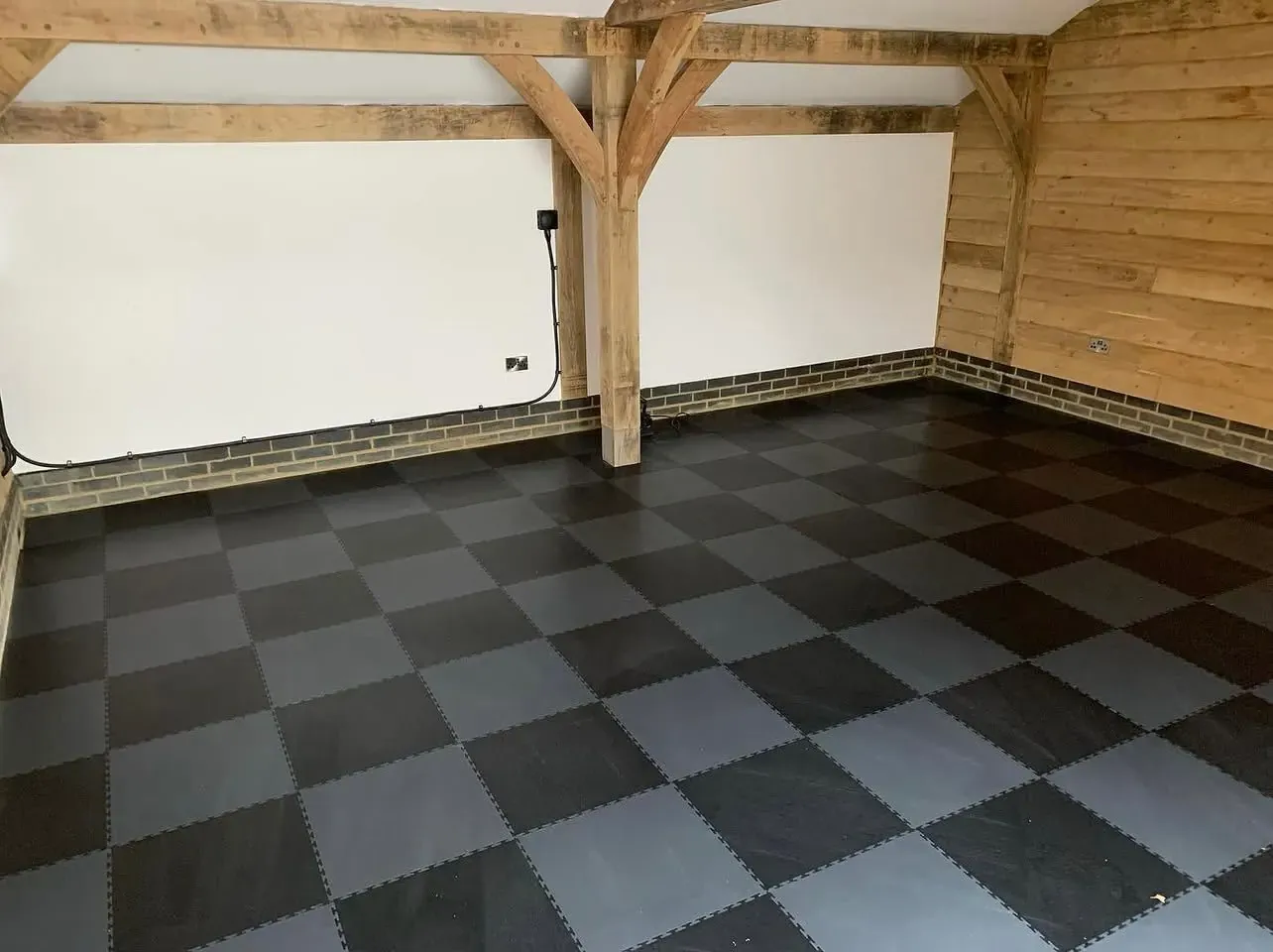 Same oak-frame garage bay finished with black and grey PVC interlocking tiles in a checkerboard pattern, ready as a home gym