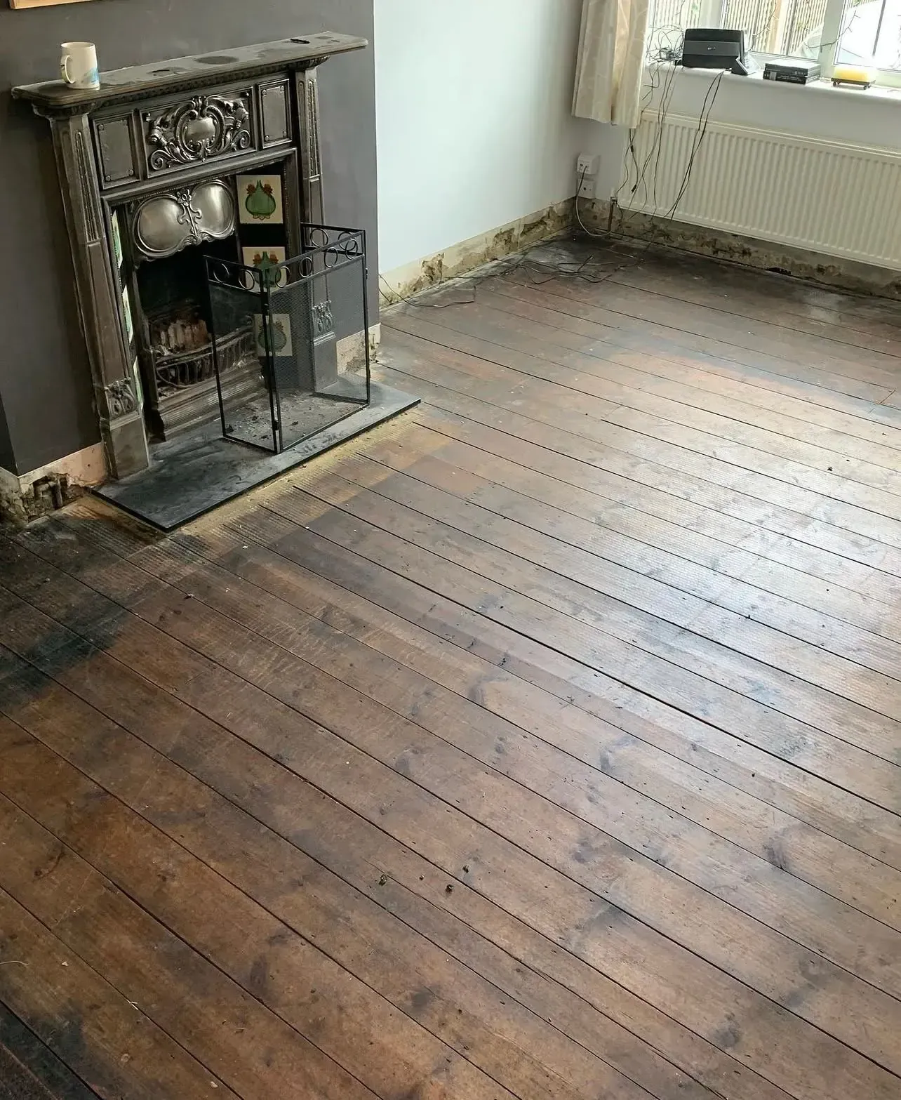 Period sitting room in Amersham with original dark-stained pine floorboards, cast-iron Victorian fireplace and exposed wiring before refurbishment