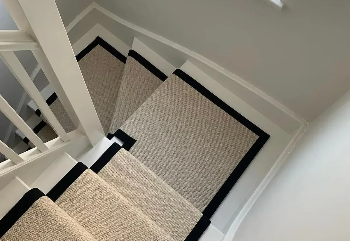Beige loop-pile stair runner with a black border fitted on a turning staircase